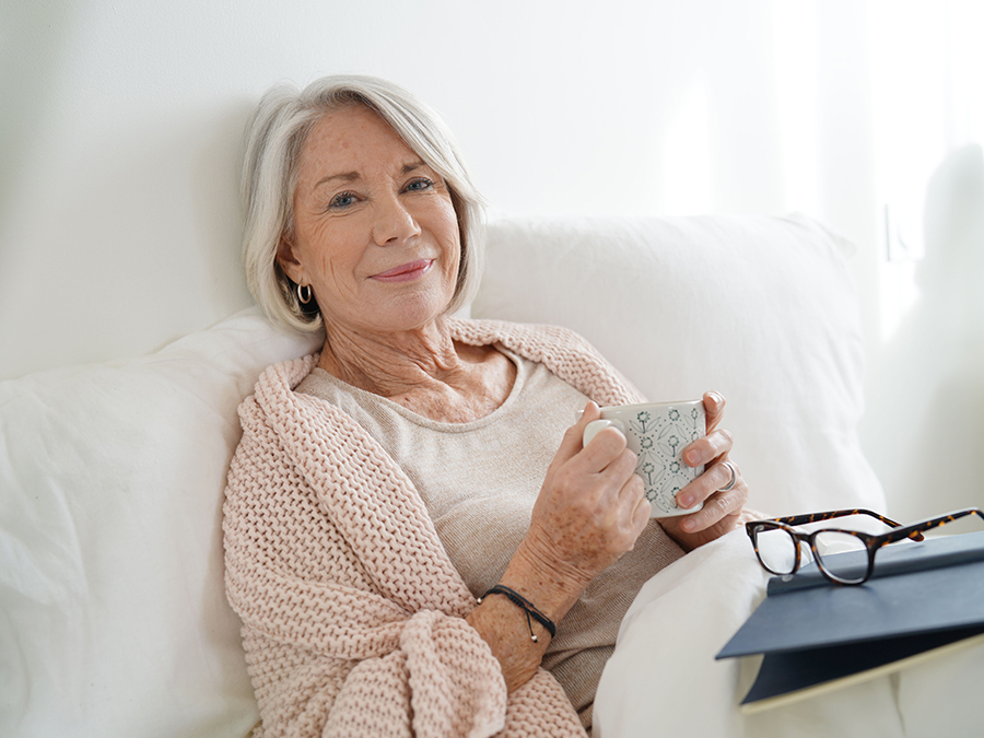 Active adult woman drinking coffee in bed relaxing with a book.